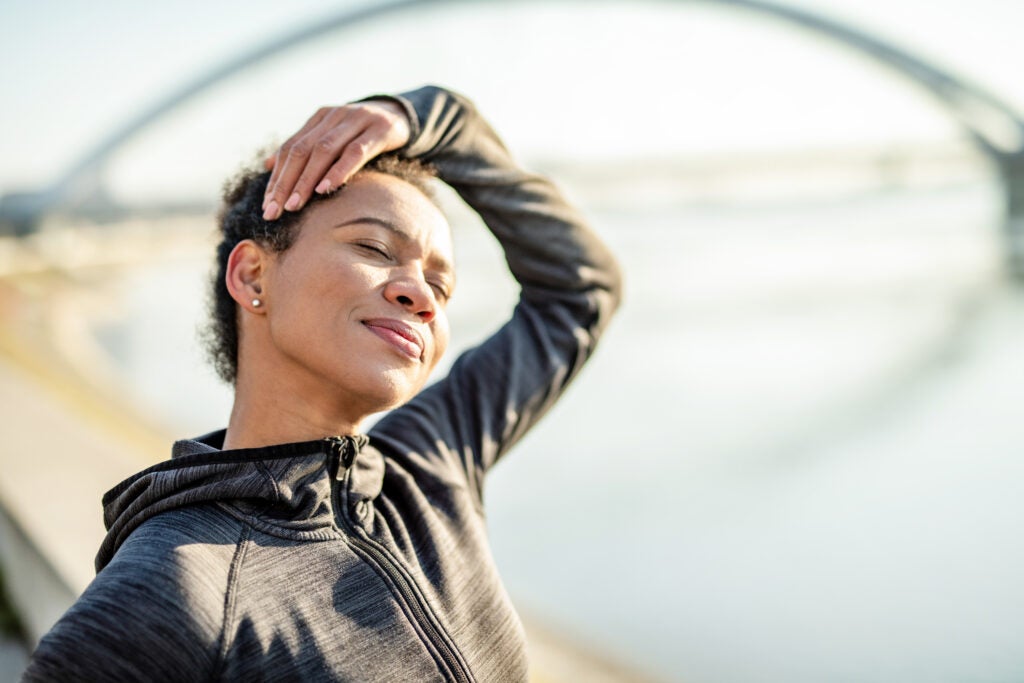Happy athletic African American woman doing neck stretching exercises outdoors.