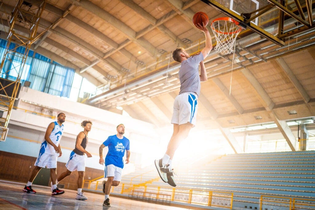 Basketball male team throwing ball into hoop while training at indoor sports court wide shot